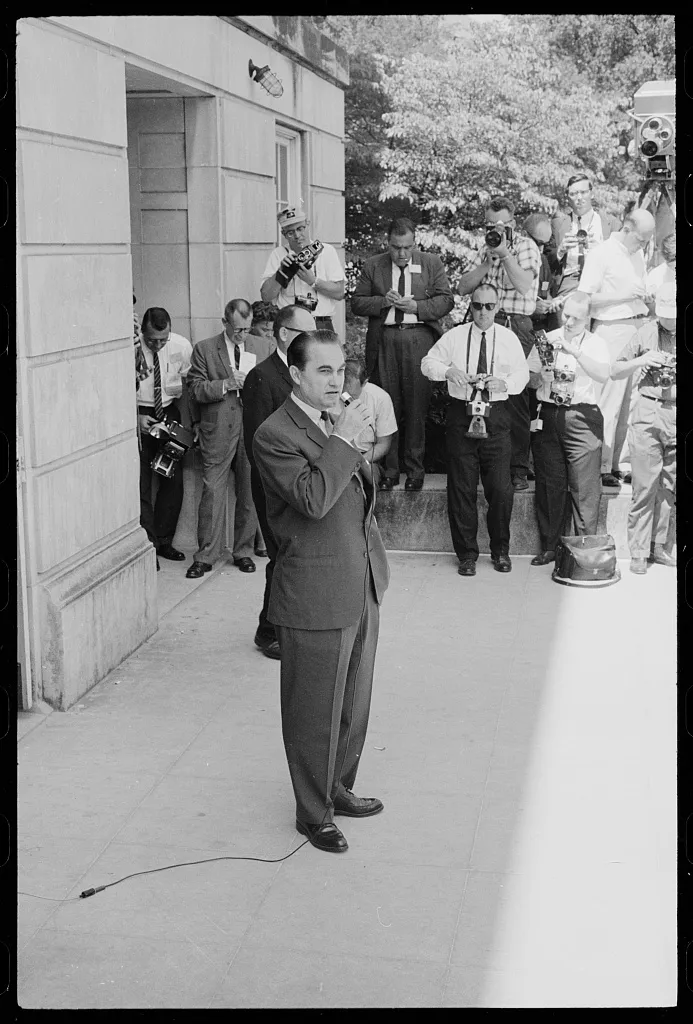 George Wallace stands outside of a building while attempting to prevent two Black students from registering