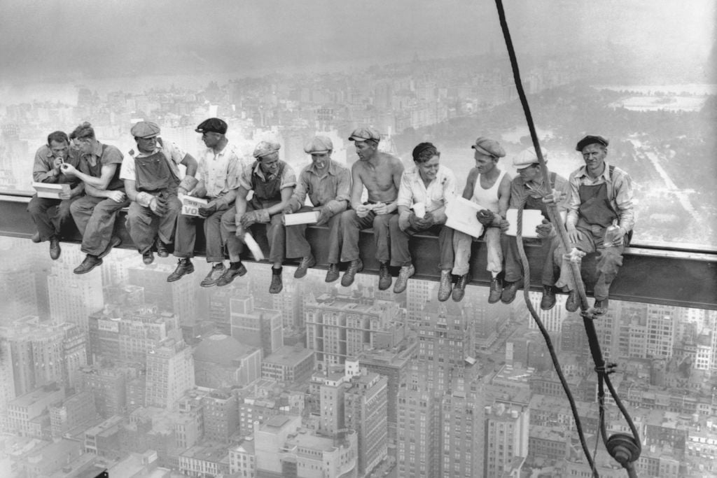 11 men sitting on a beam eating lunch above New York City