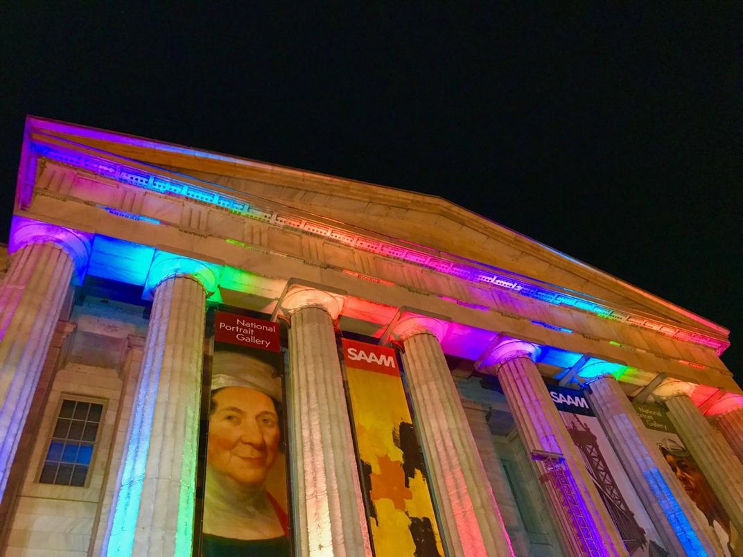 A photograph of the exterior of the Smithsonian American Art Museum at night with rainbow lights.