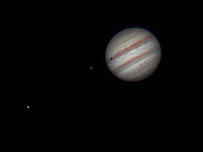 Jupiter and two moons, one casting a shadow on its surface
