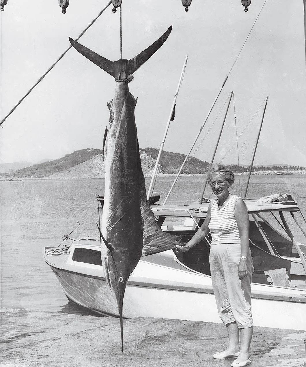 a woman poses next to a hanging marlin on a dock