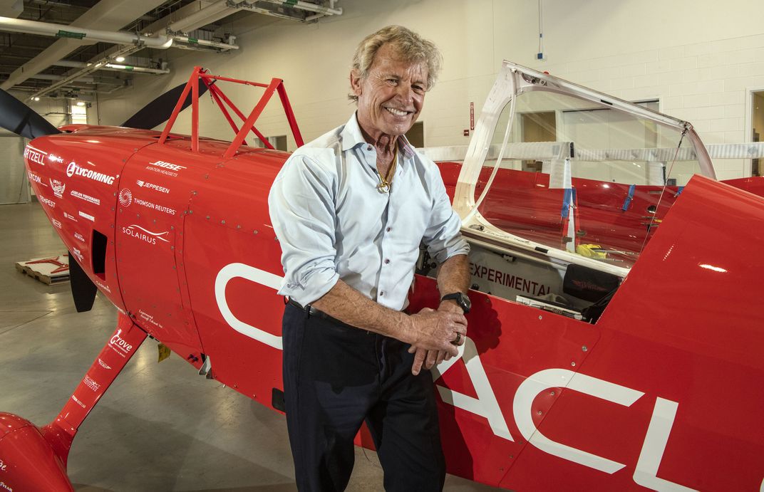 Sean Tucker leans against his red biplane.