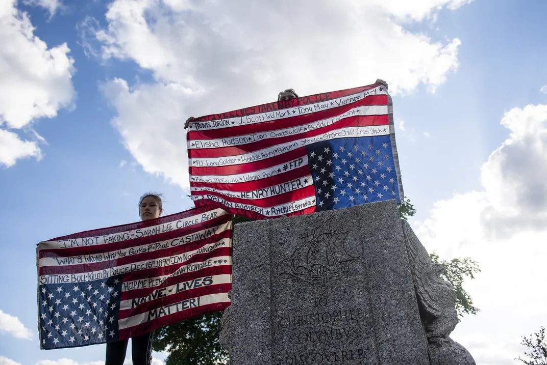 Two activists hold flags featuring the names of Native American people killed by the police.