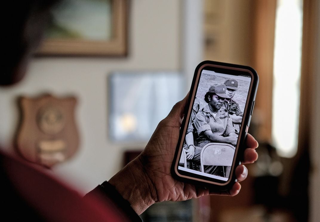 a woman holds up her phone showing a photograph of her time in the military