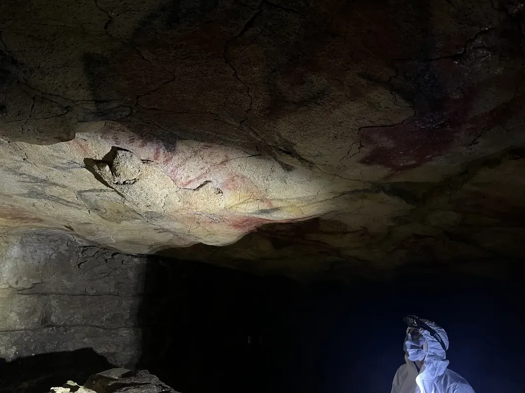 A person in a clean suit shining a light on the ceiling of a cave