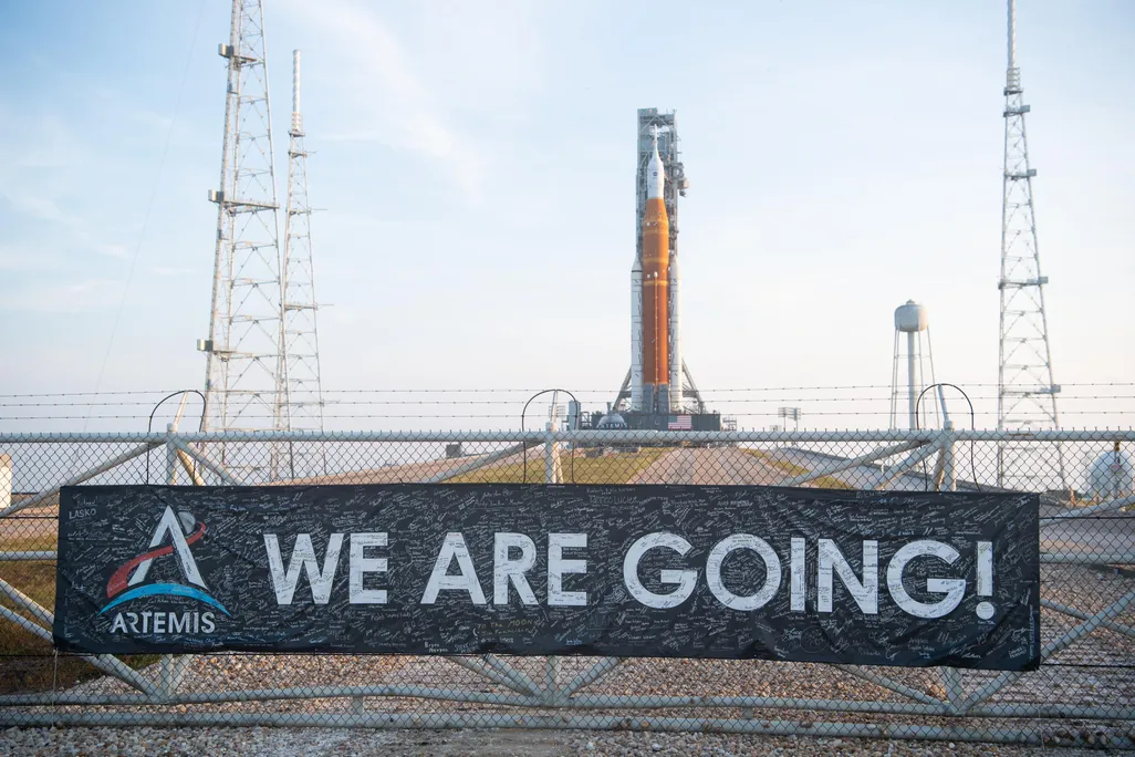 Banner on fence reads "We are going!" in front of the SLS rocket