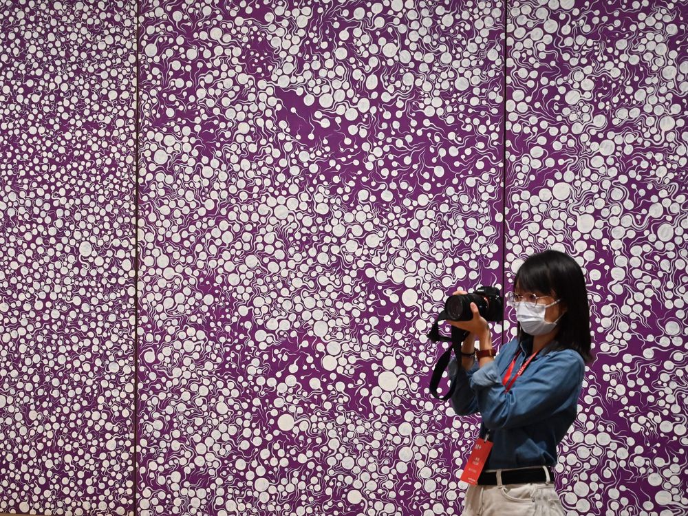 Woman wearing a mask and taking a photo in front of a purple background with white polka dots