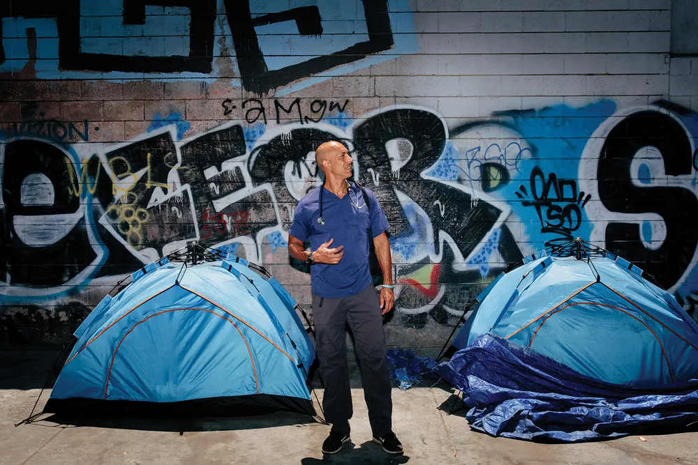 man standing in front of two blue tents and a wall of graffiti