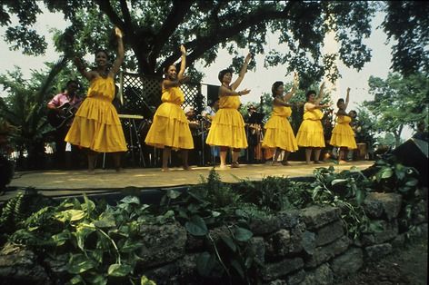 Six hula dancers in yellow dresses on a stage.