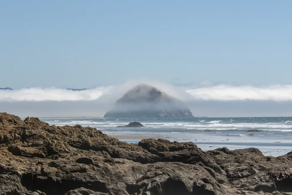 Large rock emerging from ocean with rocky coastline in foreground