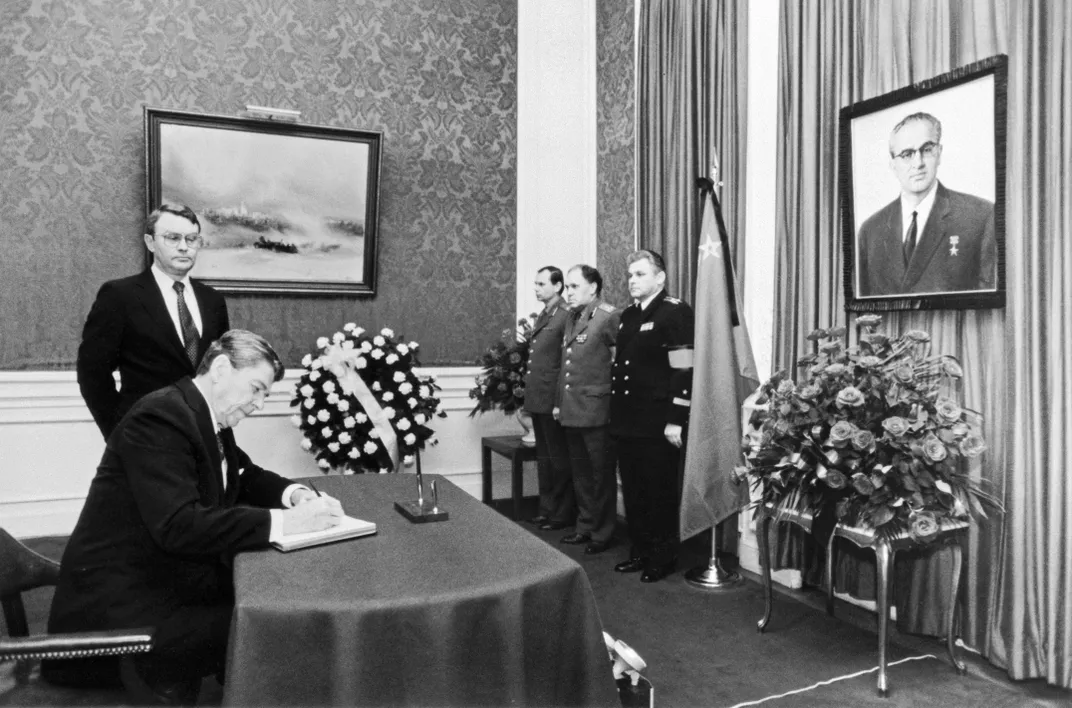 Ronald Reagan signs a message expressing his condolences on the death of Soviet leader Yuri Andropov—seen in a portrait hanging on the far right wall—in February 1984.
