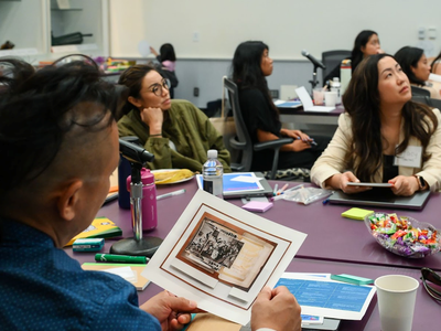 A man in a blue shirt looks at a photograph of archival images while several other people look toward a presentation