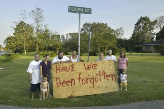 Group of people stand behind hand-painted sign reading "Have we been forgotten" 