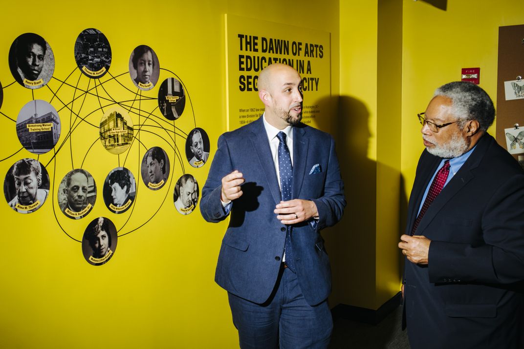 Secretary Bunch and curator Samir Meghelli talk in front of a diagram of interconnected artists and art educators.