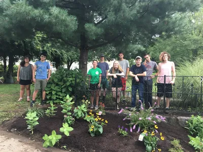 A group of young people stand in front of a pollinator garden in Lowell, MA
