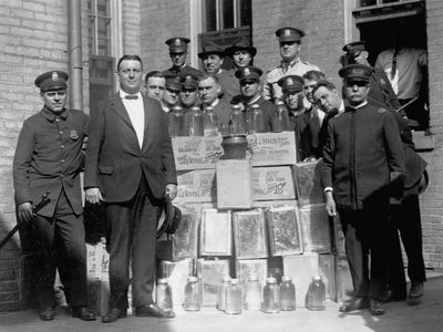 Police officers stand proudly with jars and crates of moonshine, brewed illegally duirng the prohibition. Washington, D.C.
