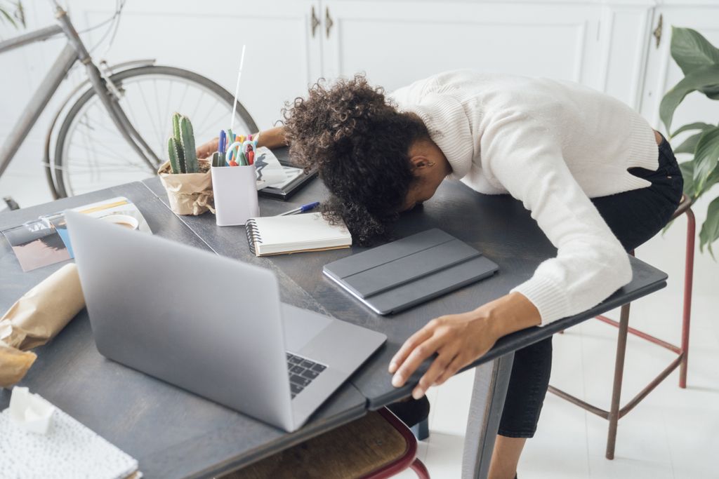 A woman puts her head down on a desk amid her laptop and notebooks