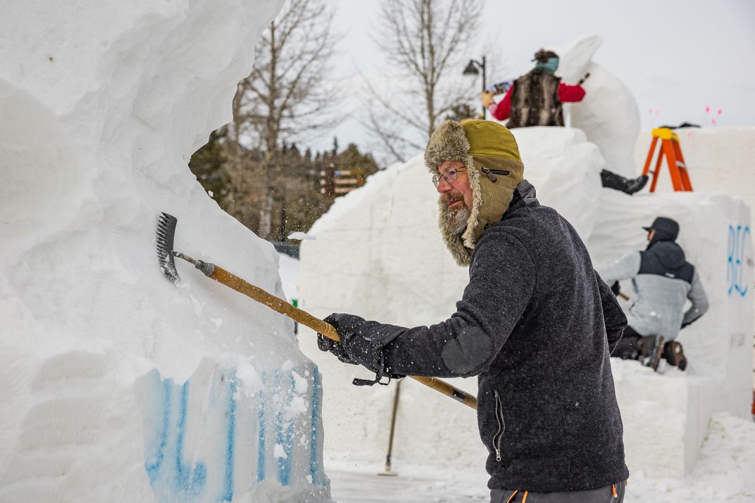 A man using a tool to carve into a block of snow