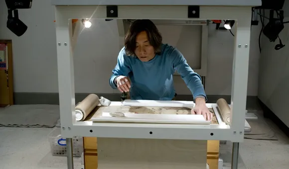 Conservator Jiro Ueda positions the handscroll prior to reflectance imaging spectroscopy. A large camera mounted above his head captures images through a hole in the table