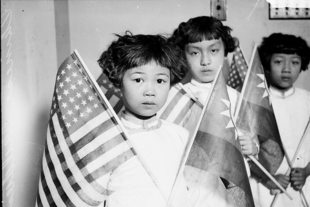 Group portrait of three Chinese children, each holding an American flag and a Chinese flag, in a room in Chicago, 1929