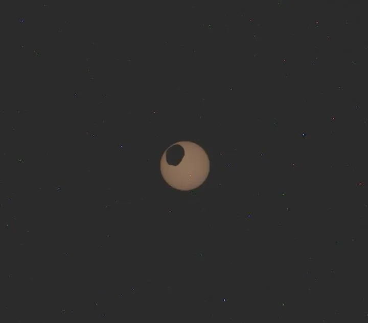 an odd oval passes across an orange sphere in the dark