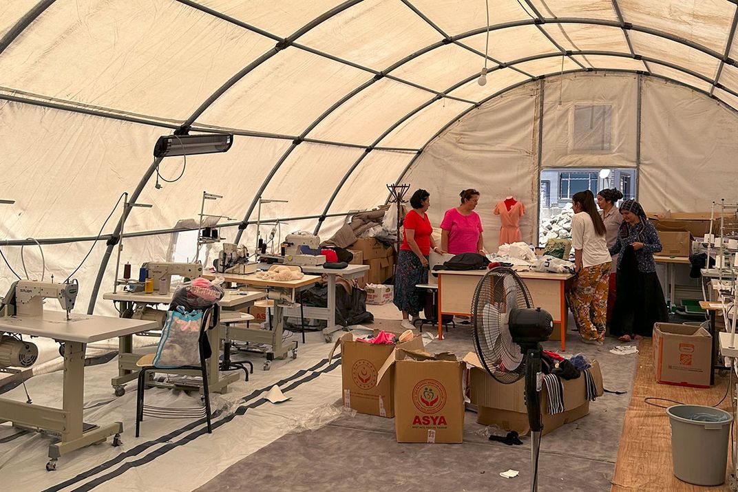 Under a white domed tent, people work among rows of industrial sewing machines.