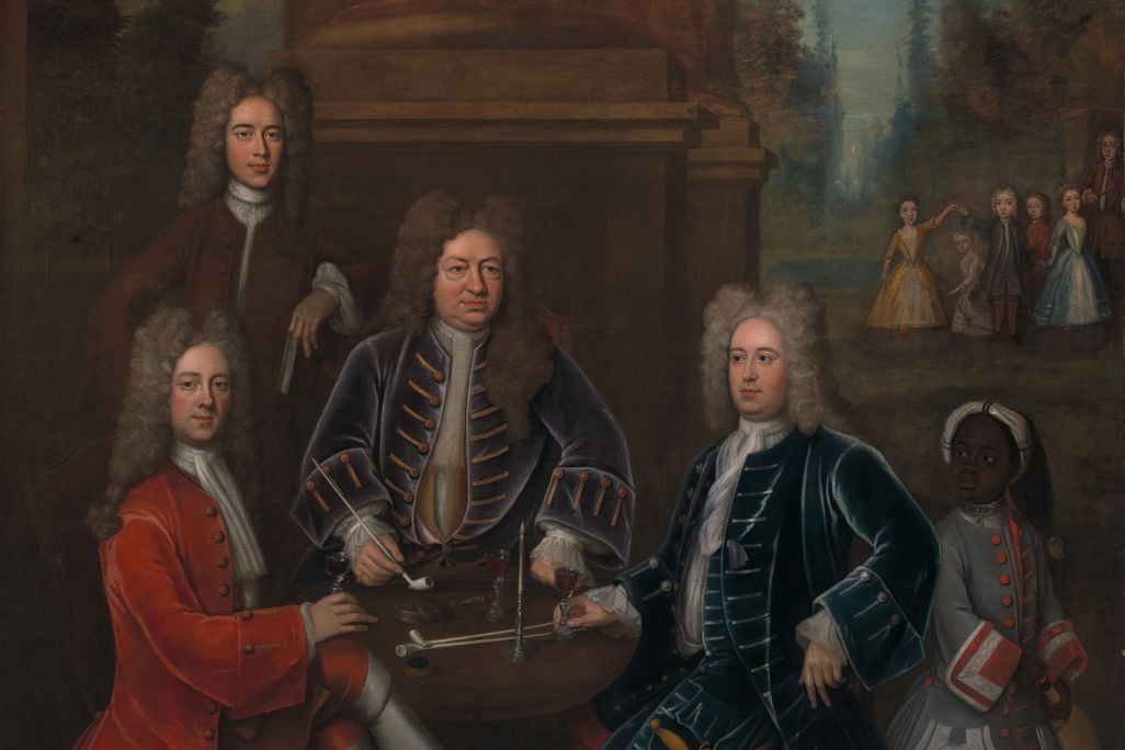 A group portrait of four white men sitting and standing around a table, smoking and drinking wine, while a small group of white children play in the distance and a Black child wearing a padlocked collar serves them wine