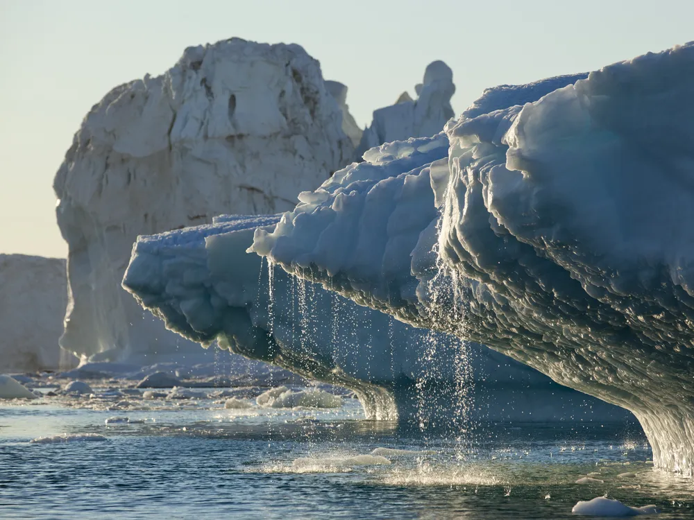 A chuck of glacier ice floating in the ocean in greenland with water running off of the ice