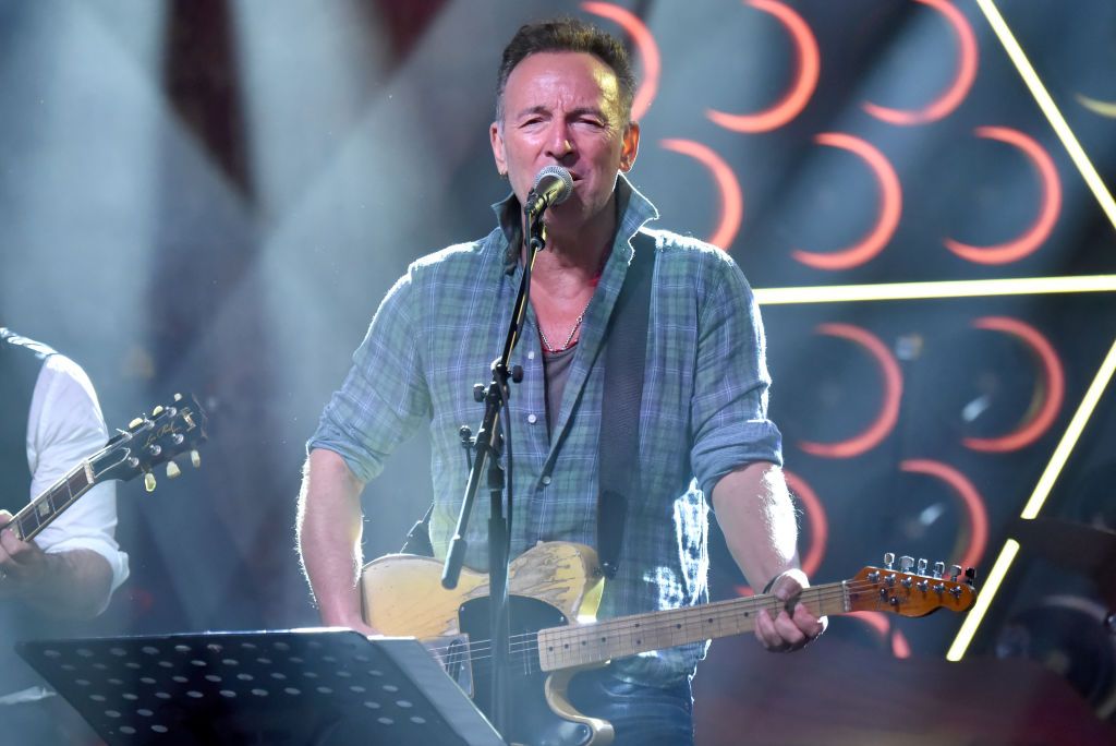 middle-aged man singing on stage into microphone and playing
