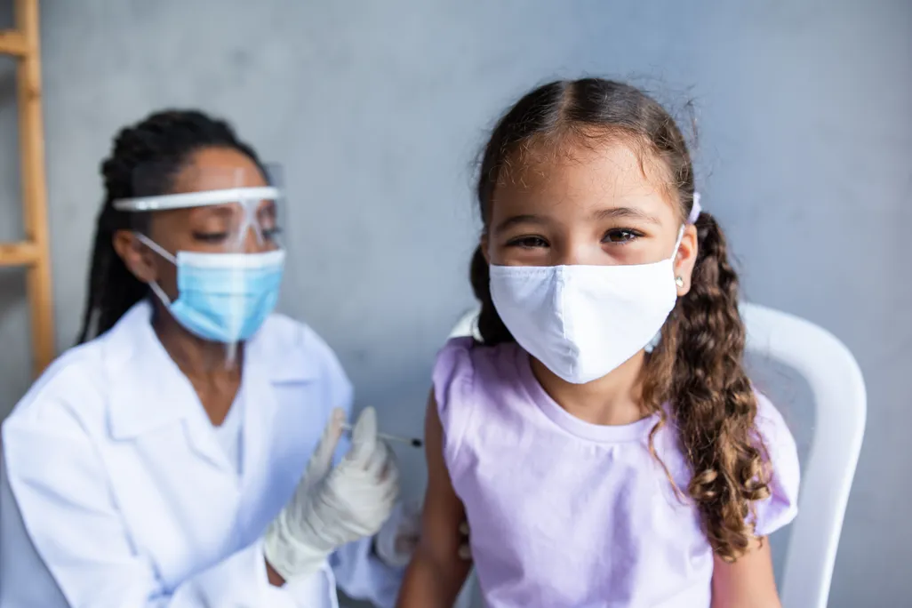 An elementary school aged girl wearing a face mask gets a vaccine