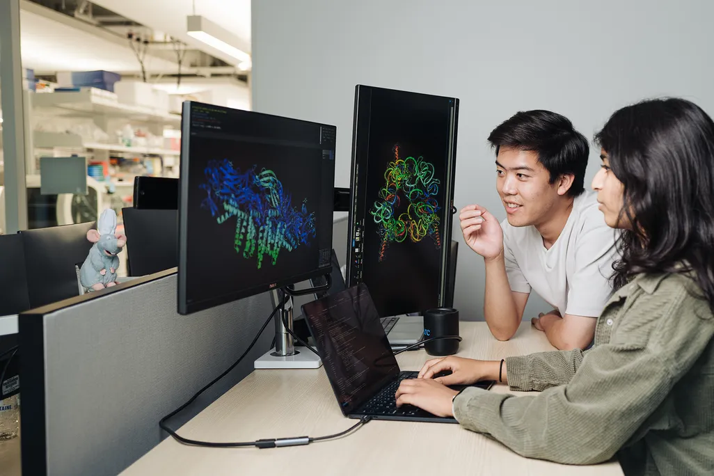 two people sitting in front of a desktop computer looking at models