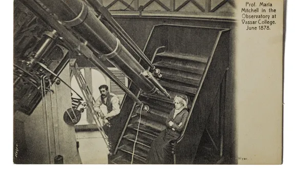 Postcard showing a woman sitting on the observing chair in front of a large refracting telescope. A man stands to her right leaning forward on a ladder.
