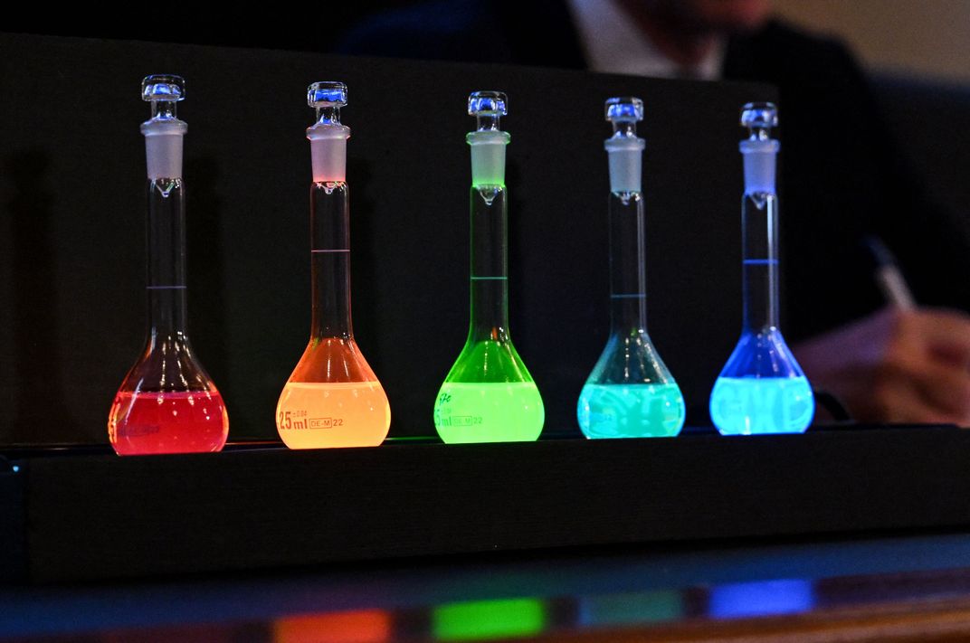 five vials with glowing matter inside. from left to right: red, orange, green, and two shades of blue