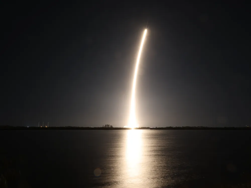 a rocket launch shows a golden streak over the water in the dark