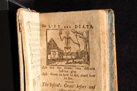 A page from a New England Primer printed in Massachusetts in 1811, with the text "Life and the Grave two different lessons give/Life shows us how to die, death how to live."