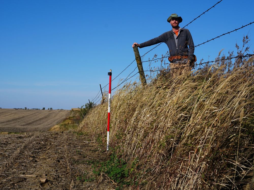 An image of a reseacher standing on native prairie a few feet above degraded farmed land.