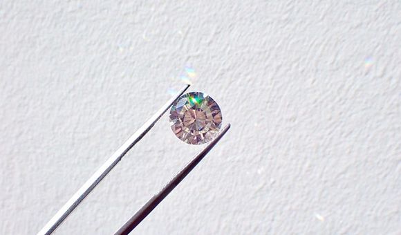 Silver tweezers hold a small diamond against a white background.
