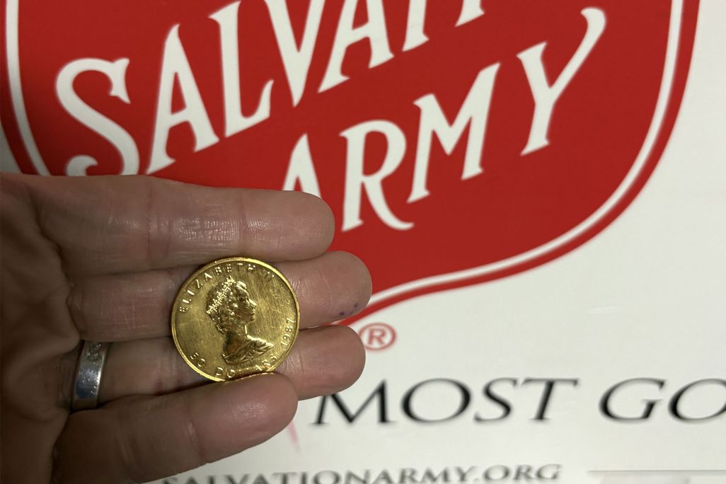 A red sign that reads The Salvation Army with a hand in front of it holding a gold coin