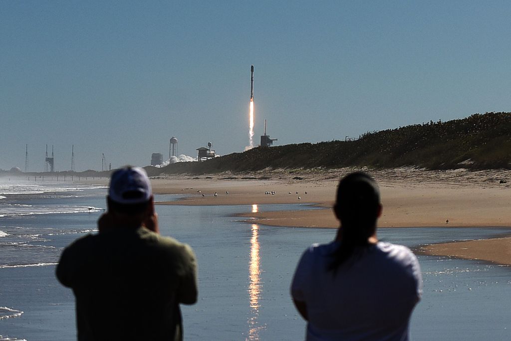 Image of SpaceX’s Falcon 9 rocket lifting off in Florida with blue sky and trail of fire, onlookers in foreground