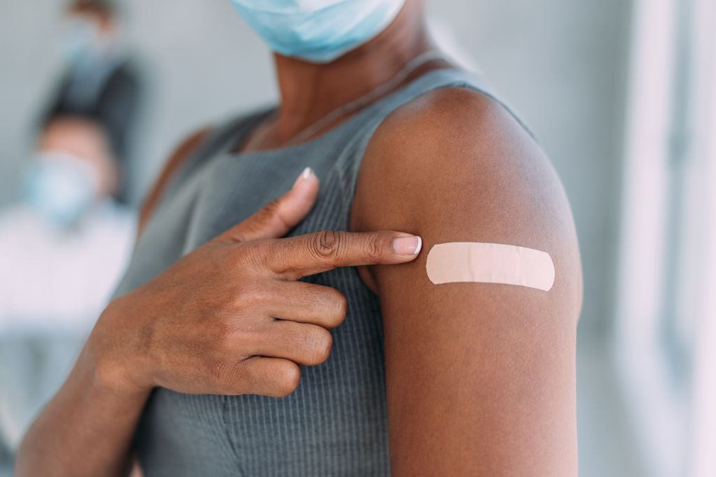 A Black woman pointing to her arm with a bandaid after vaccination