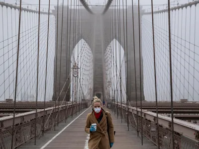 A woman wearing a mask walks the Brooklyn Bridge in the midst of the coronavirus (COVID-19) outbreak on March 20, 2020 in New York City. 