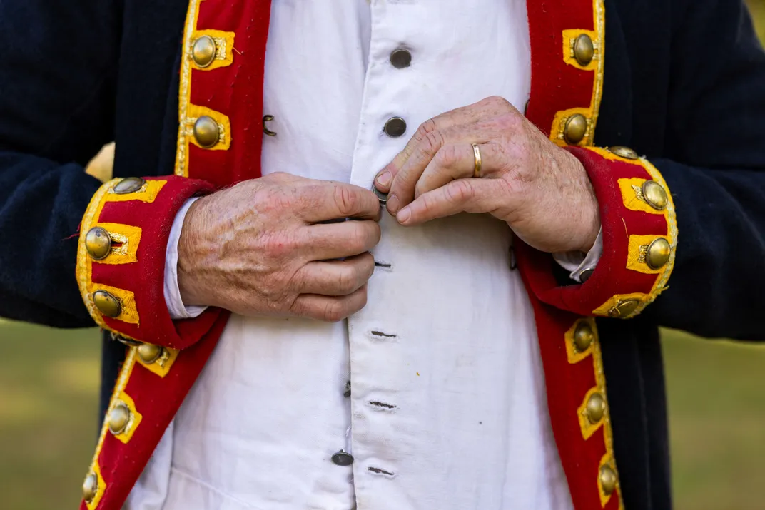 an actor buttons up a 2nd Continental Army artillerist’s waistcoat