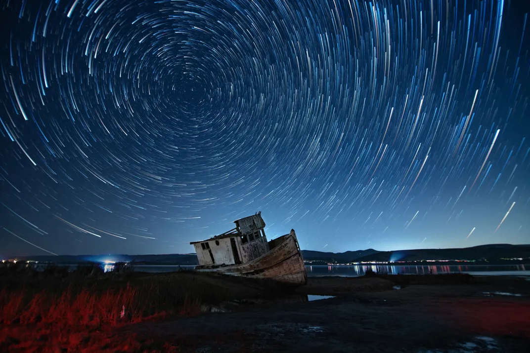 a wrecked boat with star trails above