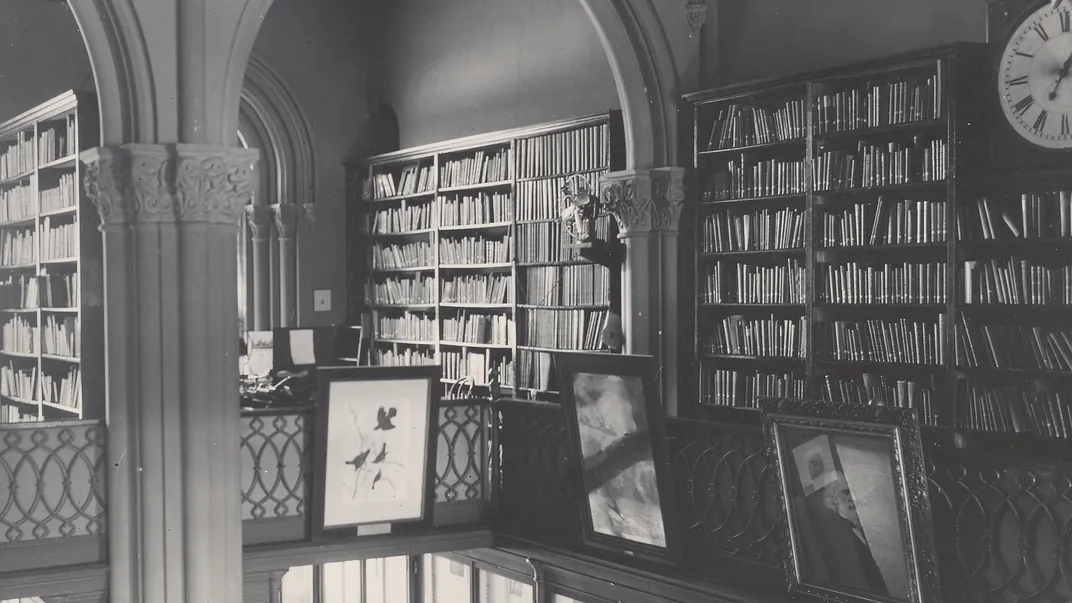 Black and white photograph of library with book shelves and frame pictures. 