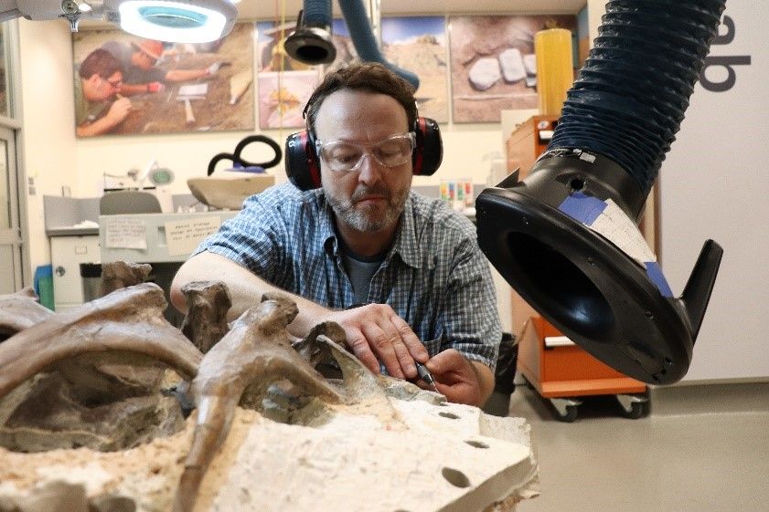 A volunteer wearing ear and eye protection as he works to free fossil bone from rock at a work bench in the Smithsonian's FossiLab.