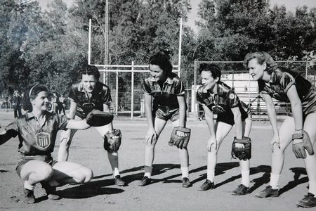 A group photo of women in softball uniforms wearing baseball gloves pose for a photo