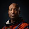 Dramatically-shot portrait of a Black male astronaut in an orange spacesuit.
