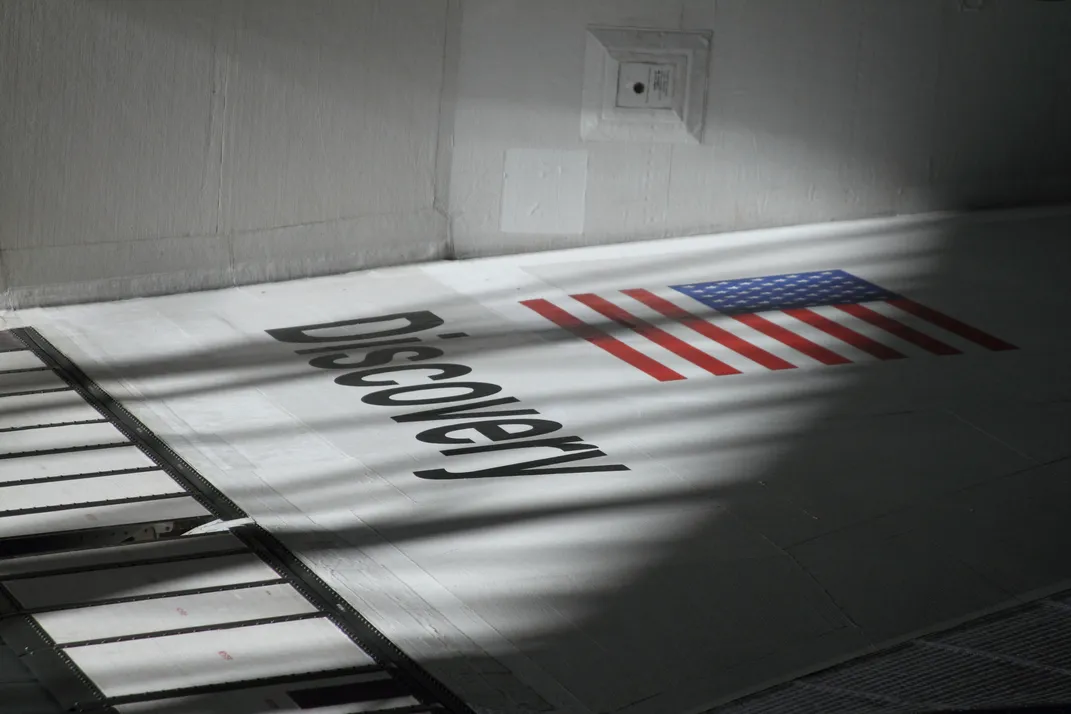 13 - Light illuminates the identifying right wing of the Space Shuttle Discovery just after its entrance into the space hangar at the Steven F. Udvar-Hazy Center.