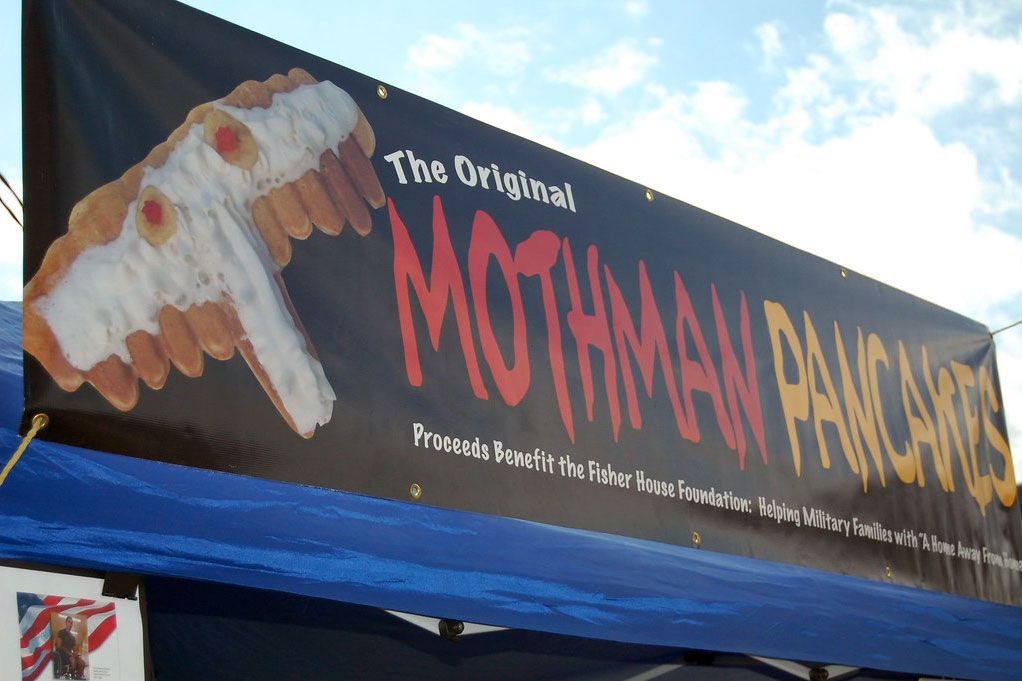 A billboard advertises “The Original Mothman Pancakes,” with a pancake in the shape of a T, covered in white whipped cream, and two red eyes.