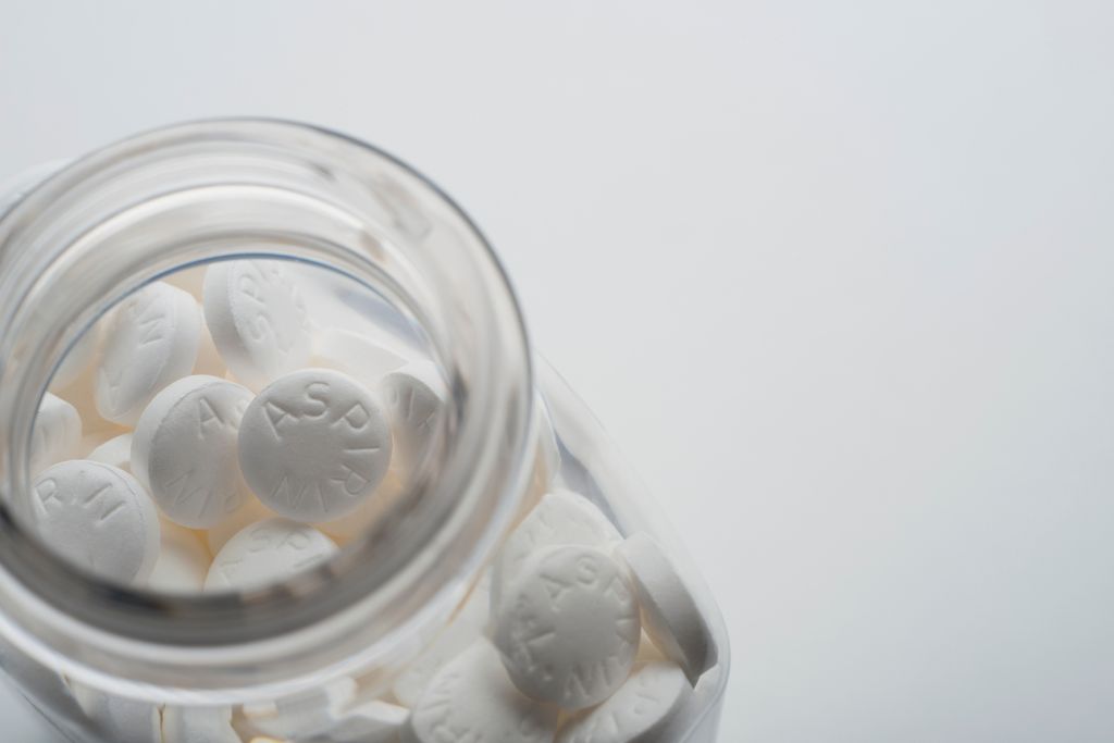 An image of a glass bottle filled with white tablets of aspirin. The bottle is shown from the top and is against a white background.